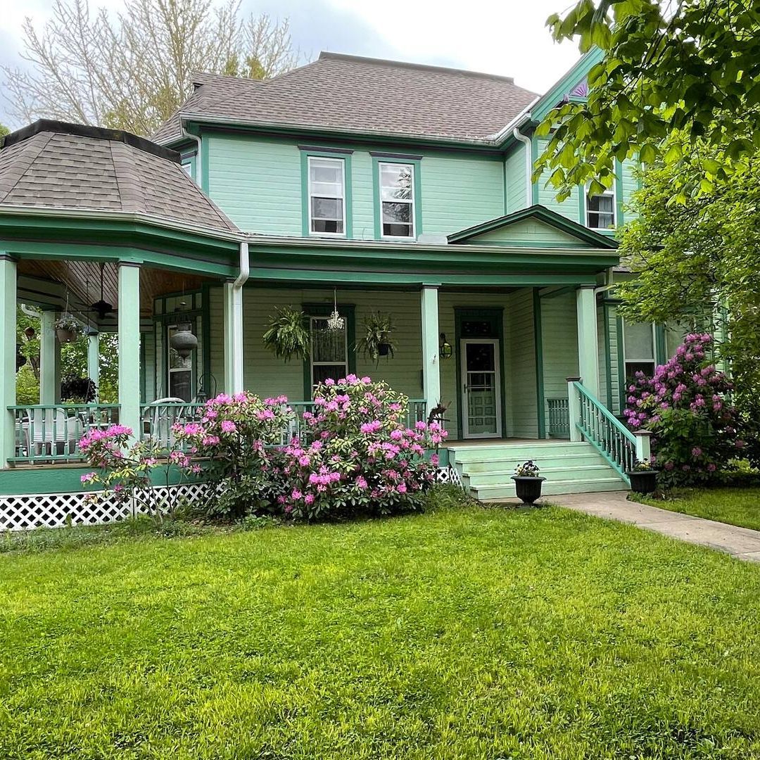a green house with a porch and flowers in front of it .