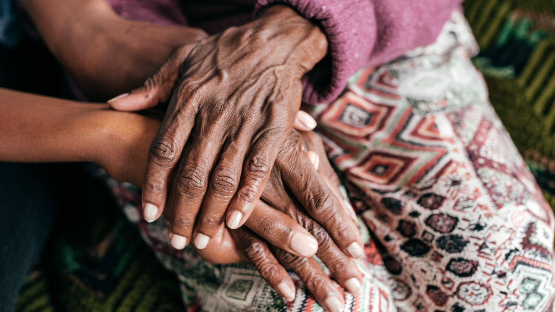 Two pairs of hands clasped together, one older with wrinkles and one younger.