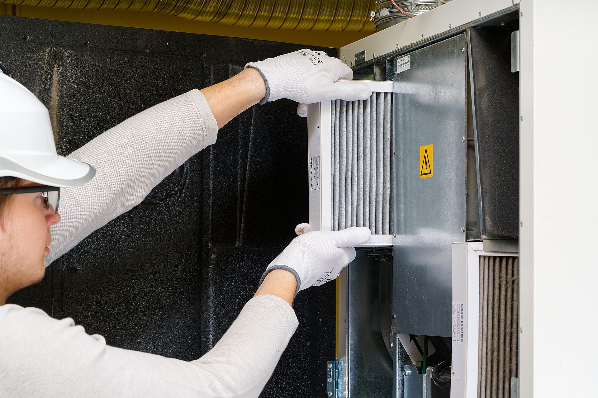 A person wearing gloves inserts a pleated white air purifier filter into a machine.