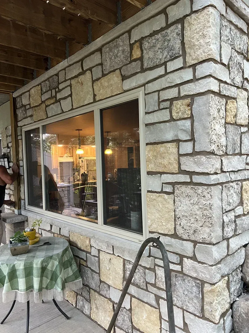 A stone wall with a large window and a table in front of it.