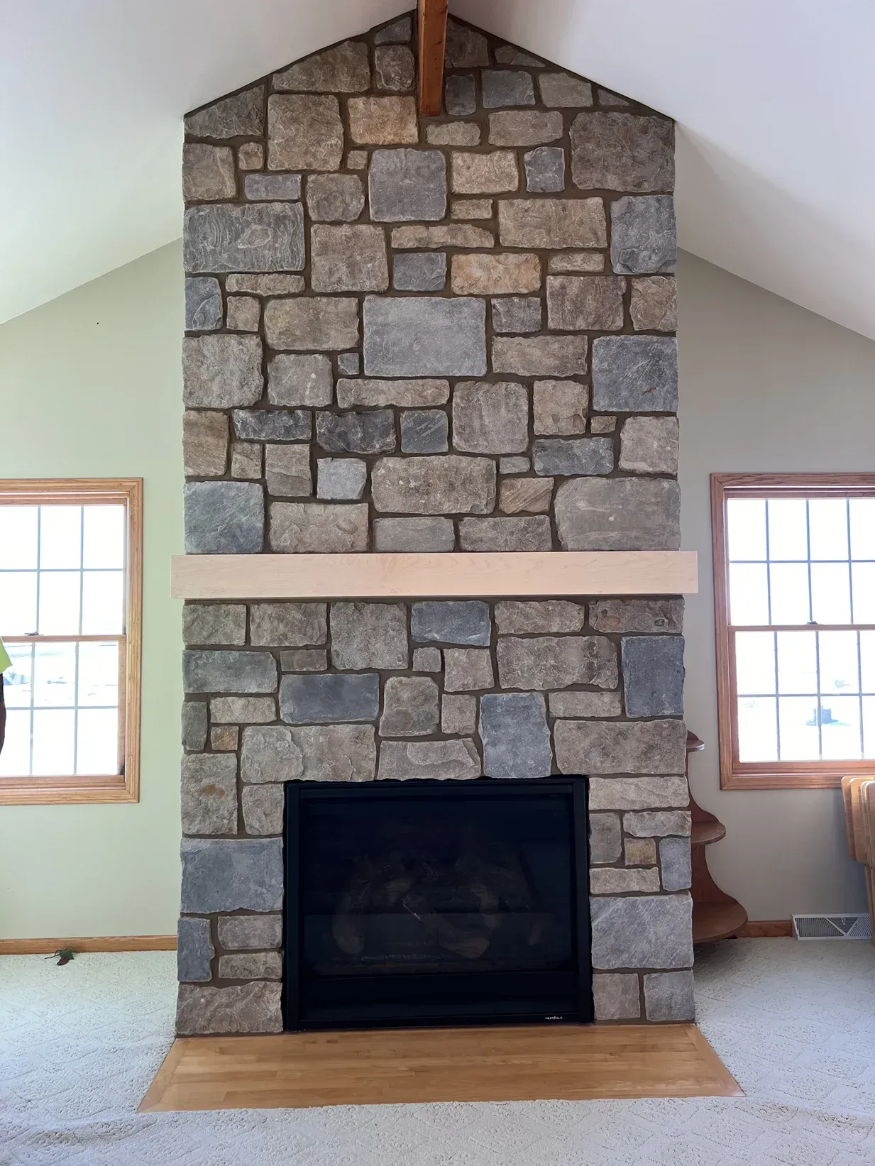 A stone fireplace in a living room with a vaulted ceiling