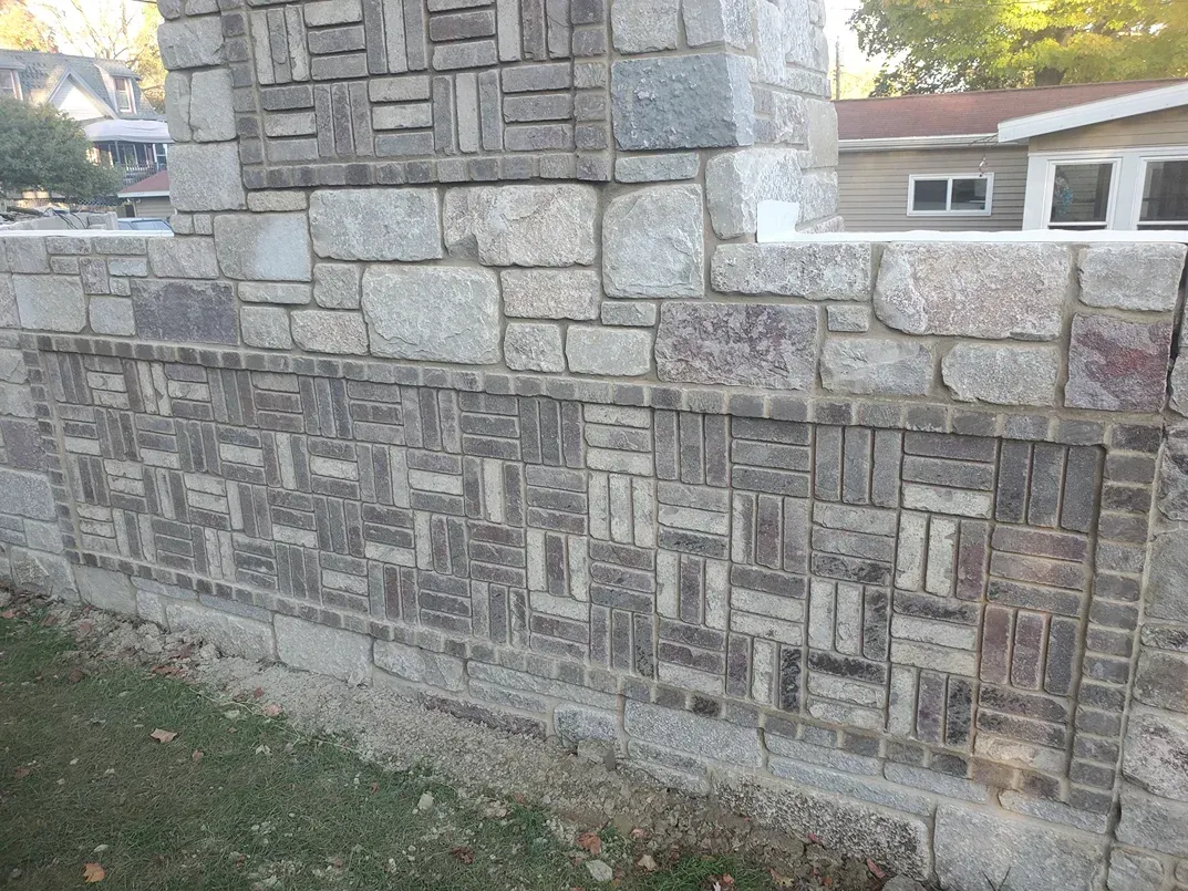 A large stone wall with a house in the background.