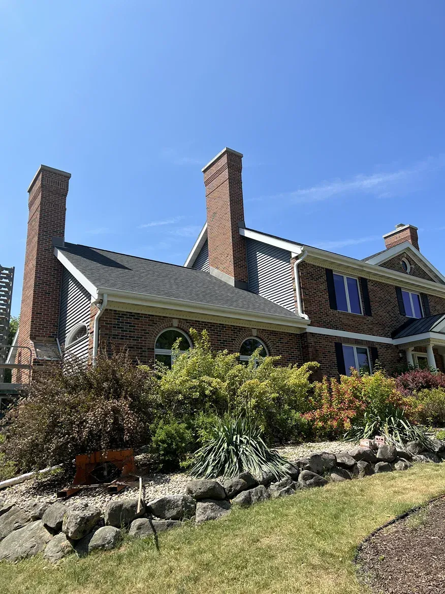 A large brick house with two chimneys and a lush green yard.