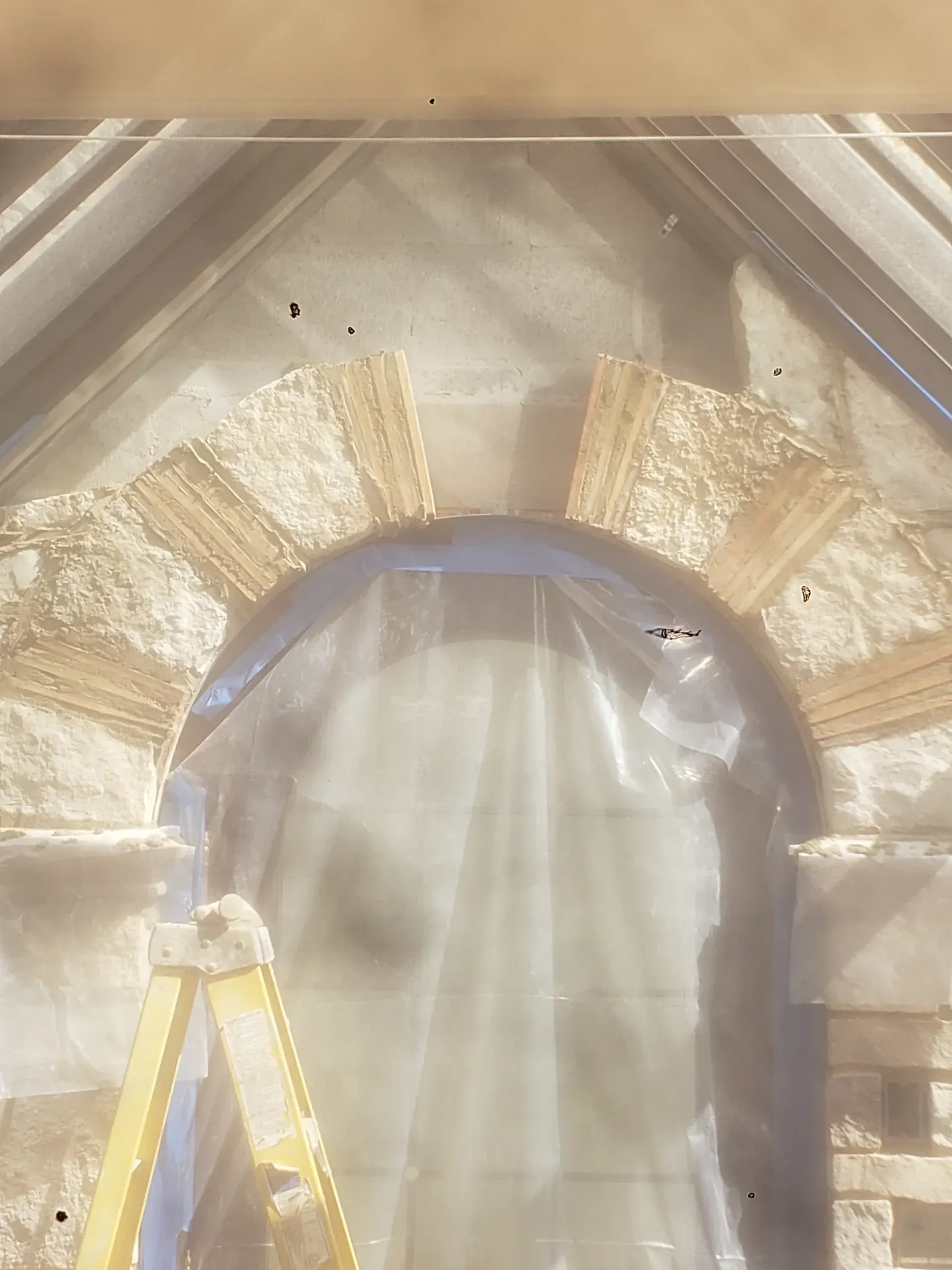 A yellow ladder is sitting in front of a stone arch covered in plastic.