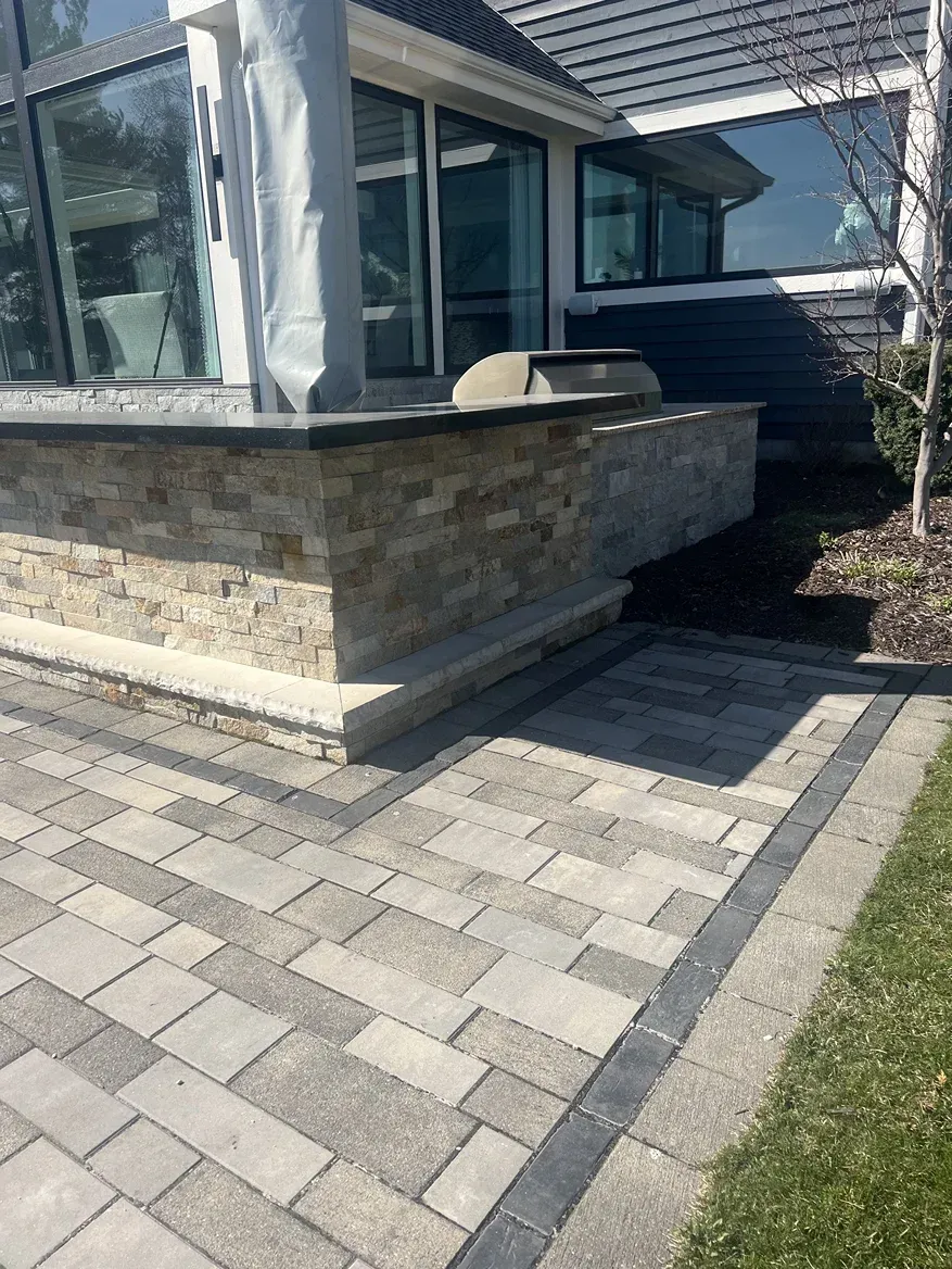 A brick walkway leading to a house with a grill on the side of it.