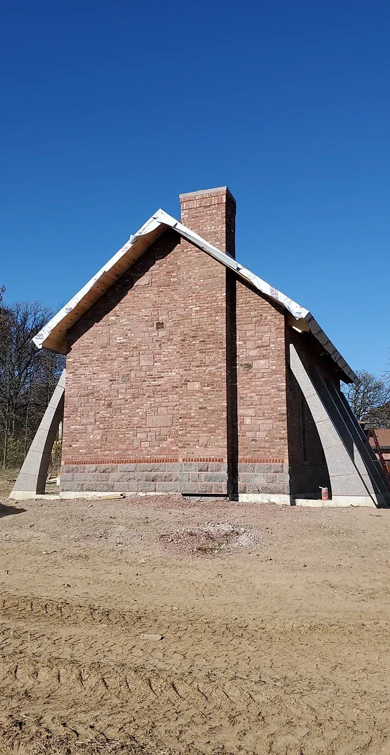 A brick house with a chimney on the side is sitting on top of a dirt field.