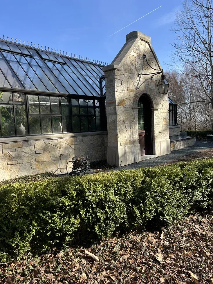 A greenhouse is surrounded by bushes and leaves on a sunny day.