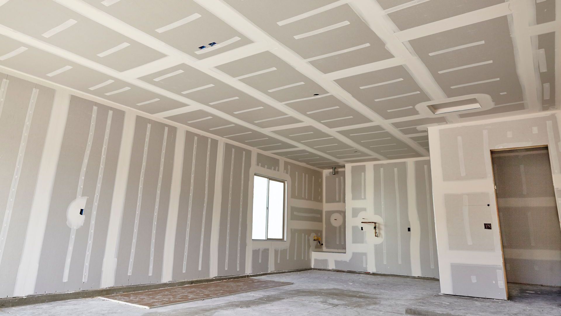Interior of a room under construction, drywall installed on walls and ceiling.
