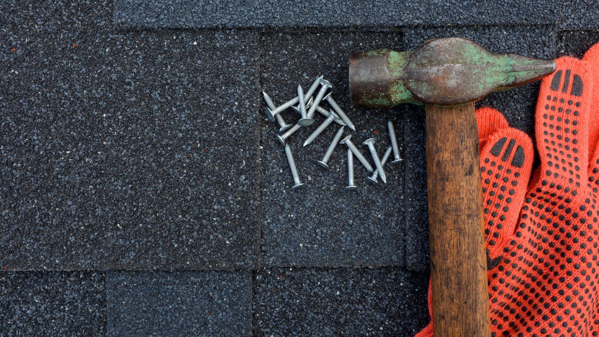 Hammer, nails, and red work glove on black asphalt shingle material.