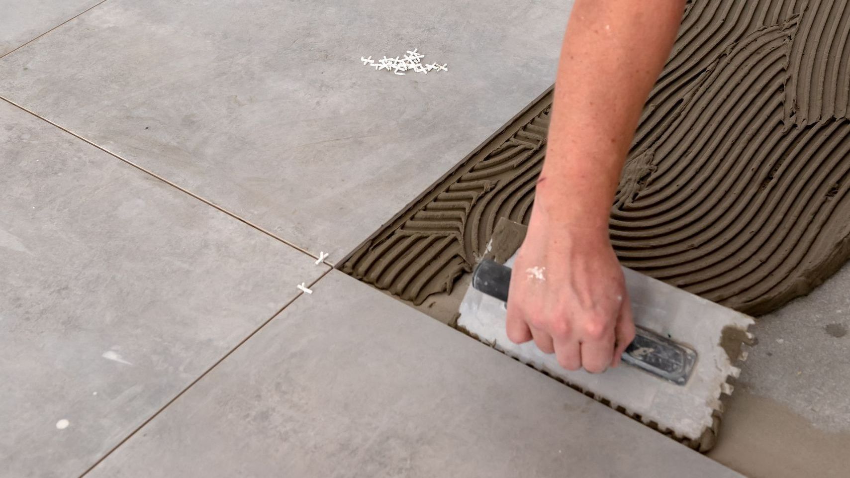 Person using a notched trowel to spread adhesive on a floor for tile installation.