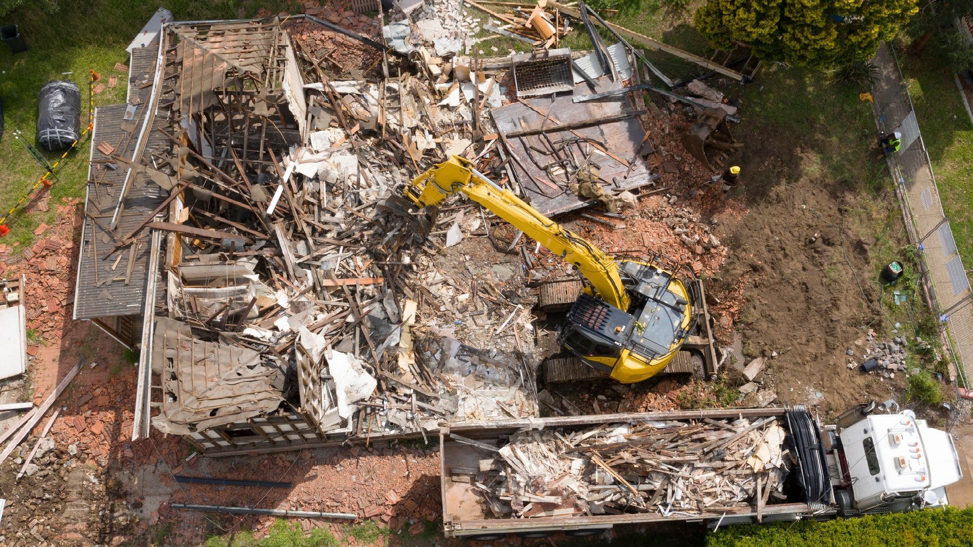 Demolition of a house, excavator loading debris into a truck.
