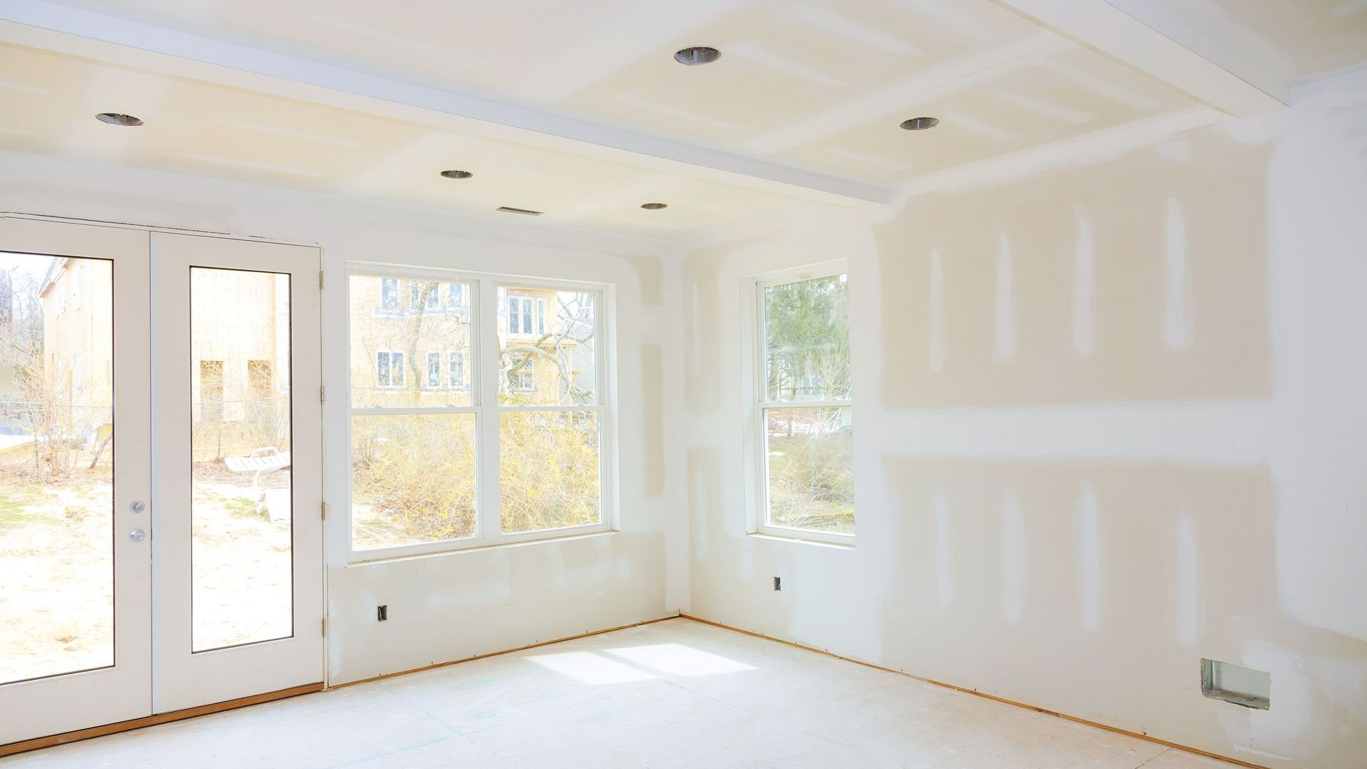 Interior room in construction with drywall walls and ceiling, windows, and recessed lighting.