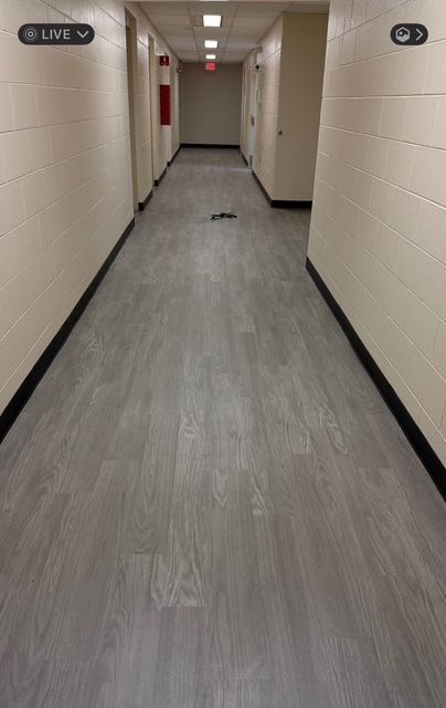 Hallway with gray flooring, white walls, and doors along the sides, leading to a red fire extinguisher and an exit sign.