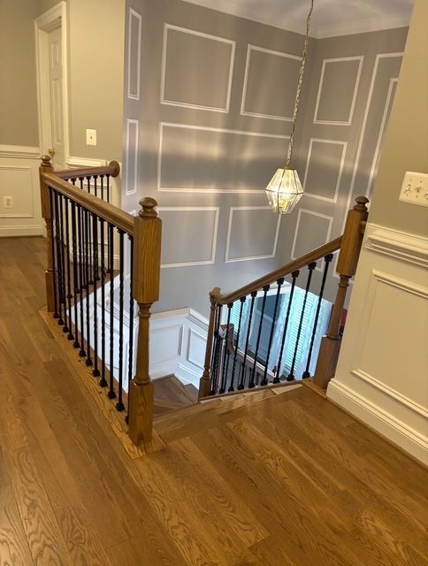 Staircase with wooden handrails, black spindles, and gray walls with white paneling.