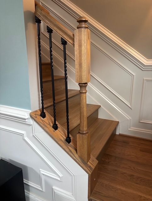 Wooden staircase with black metal balusters, tan treads, white paneling, and a blue wall.