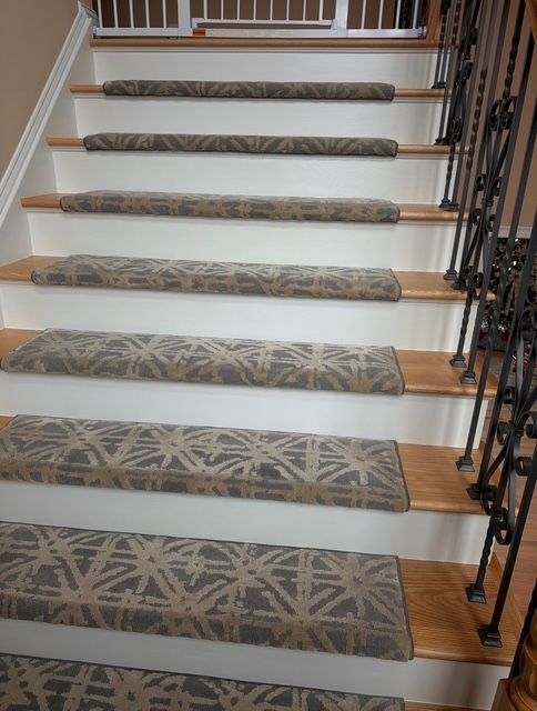Staircase with wooden steps and beige patterned carpet treads; black wrought-iron railing.