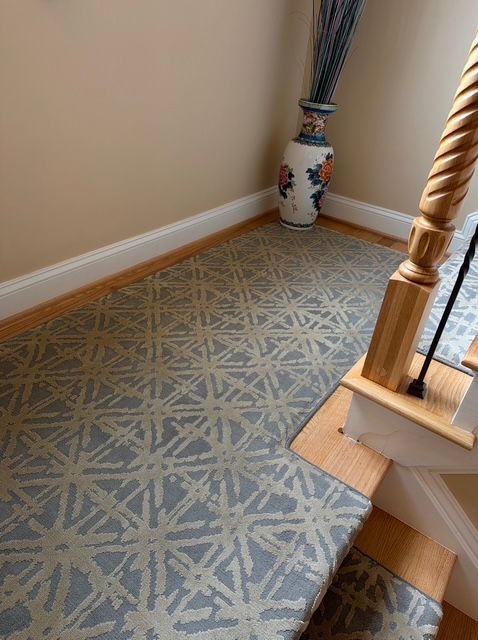 Staircase with patterned blue and beige carpet, beige walls, and a decorative vase.