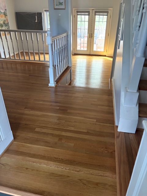 Wooden floor hallway with stairs on the right. Natural light from French doors at the end.