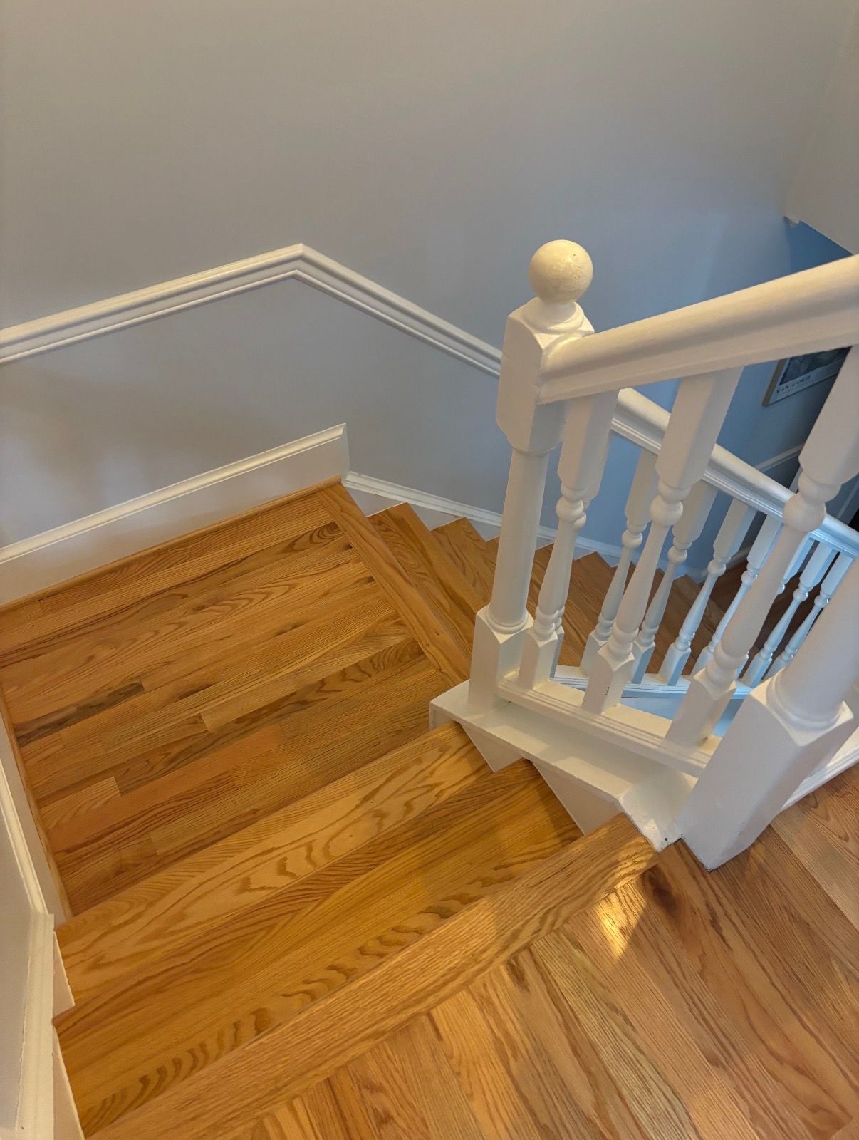 Wooden staircase with white banister, ascending against a light blue wall.