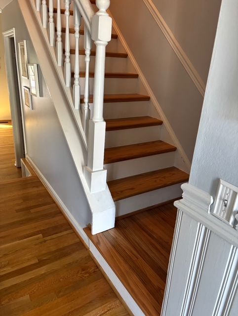 Wooden staircase with white banister, light gray walls, and hardwood floors.