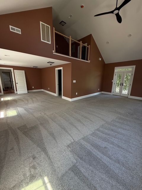 Spacious empty room with brown walls, gray carpet, and a balcony. White trim surrounds windows and doors.