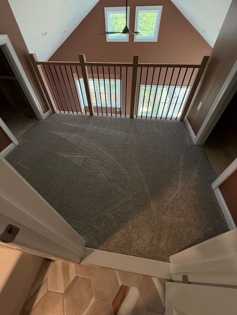 Overhead view of a carpeted loft area with a railing and two windows in the peaked wall.