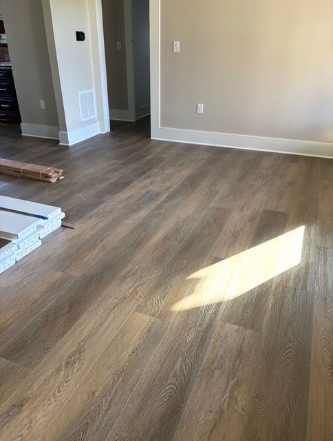 Light brown wood-look flooring installed in a room with white trim and beige walls. Sunlight shines across the floor.