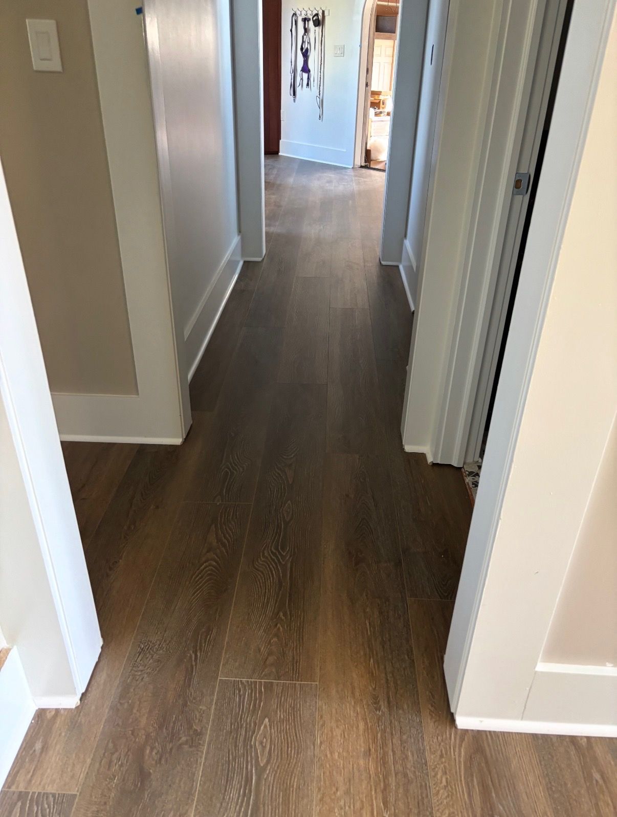 Hallway with brown wood-look flooring, beige walls, and white trim.  Doors lead to other rooms.