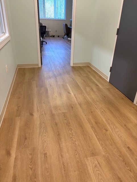 A hallway with light wood-look flooring and light green walls leading to an office.
