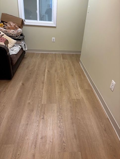 Room with light wood-look flooring, beige walls, small window, and a partial view of a couch.