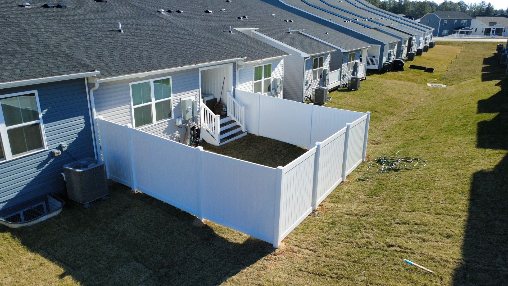 White fenced backyard with a patio leading to a row of townhouses with gray roofs.