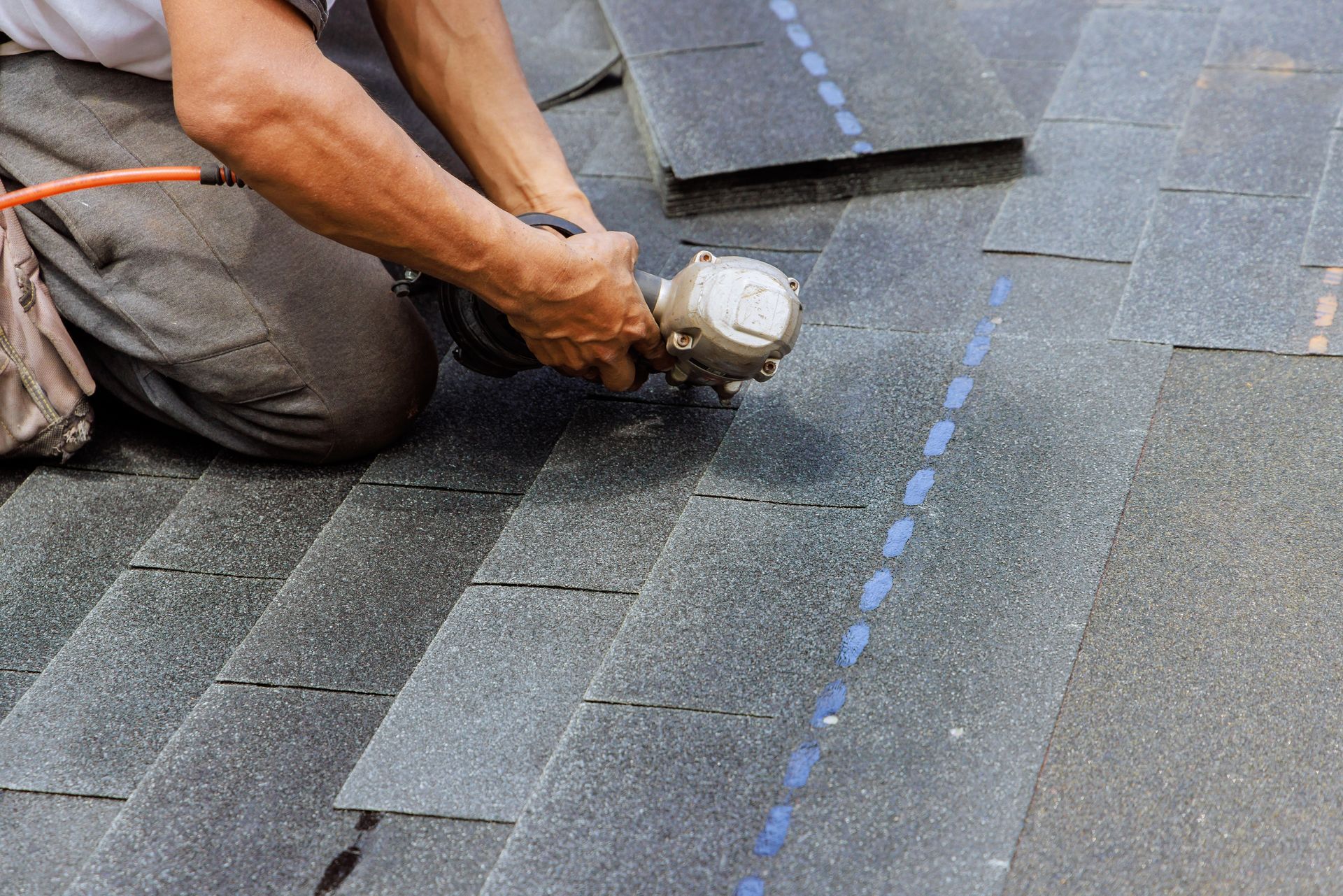 Roofer using a nail gun to install asphalt shingles on a roof.