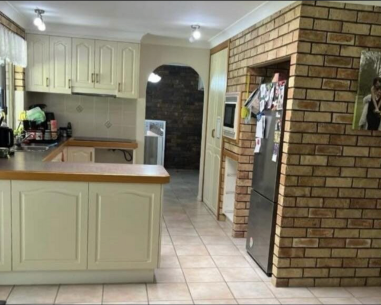 A kitchen with a brick wall and white cabinets.