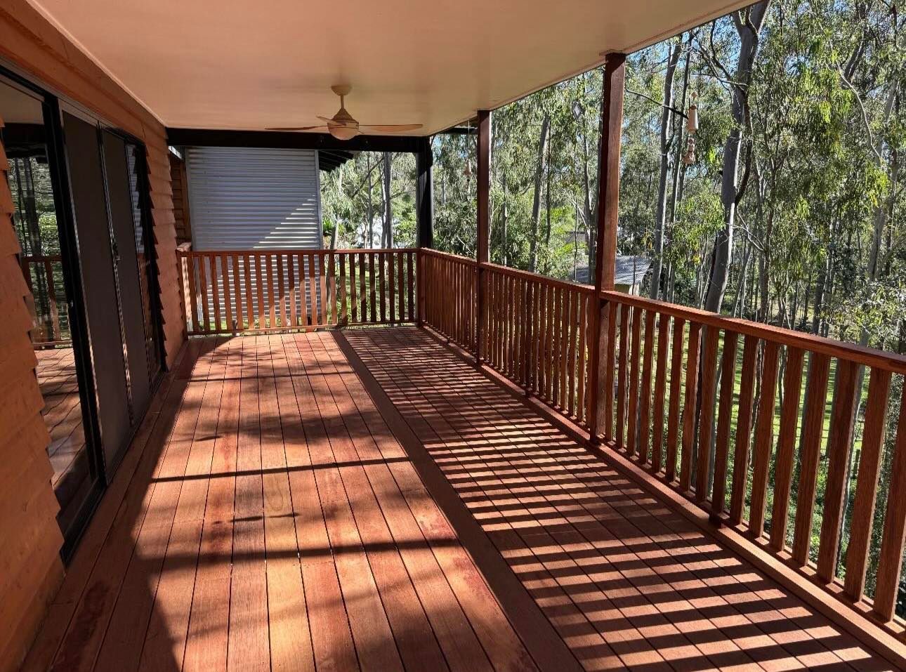 A large porch with a wooden railing and trees in the background