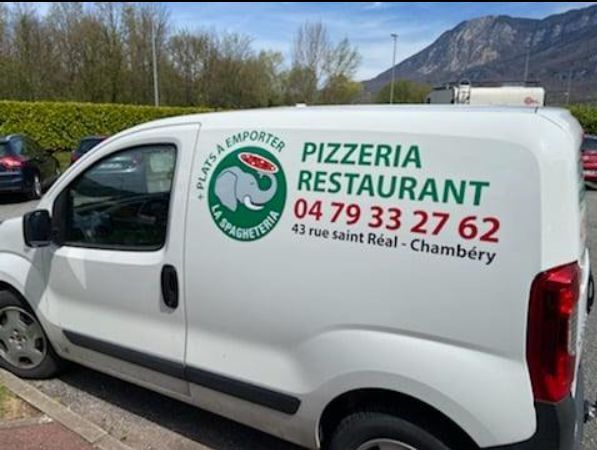 Camionnette de livraison blanche avec logo de pizzeria vert et rouge, numéro de téléphone et adresse.