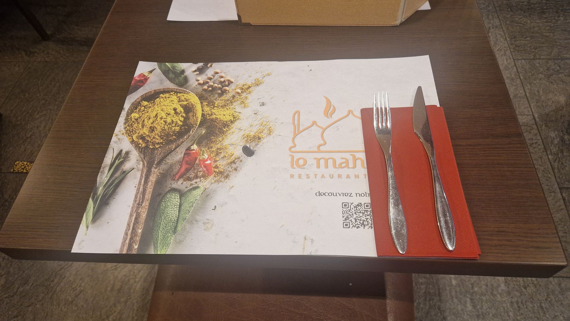 Deux tabliers, gris et bordeaux, avec un logo, accrochés sur un fond blanc.