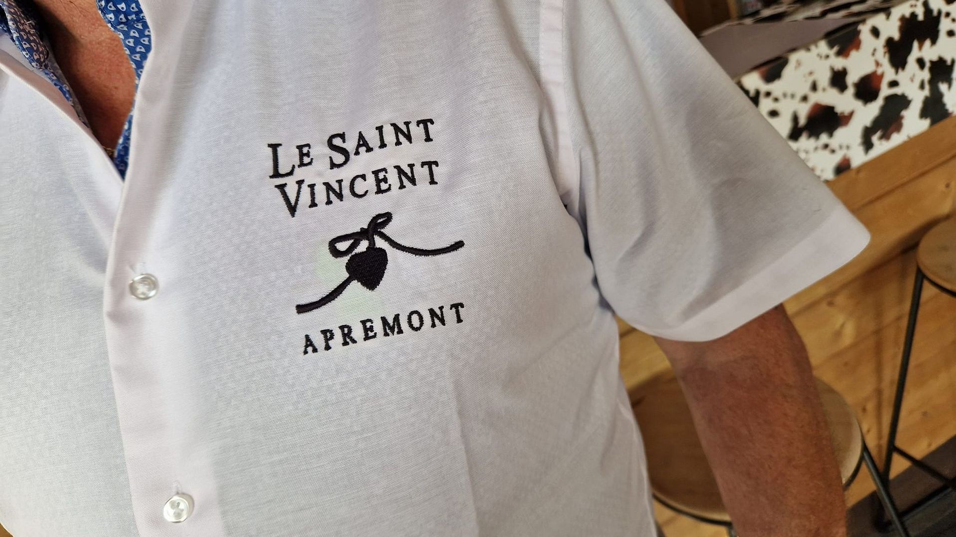 t-shirt blanc brodé avec un logo et du texte. Sur le côté gauche de la poitrine du vêtement, on peut lire 