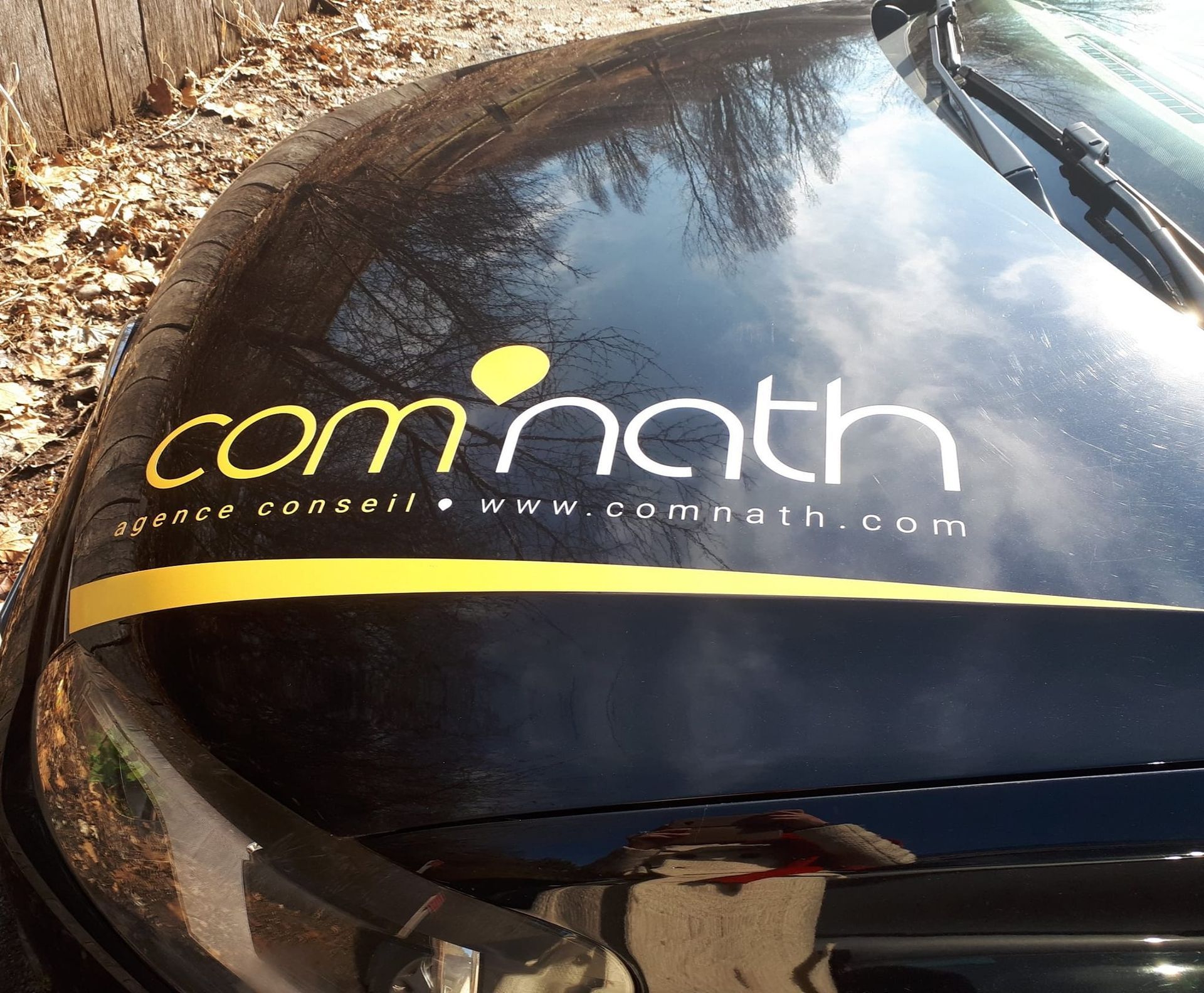 Capot de voiture noir avec logo « com'nath », bande jaune et adresse du site Web.