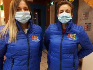 Une table dressée dans un restaurant avec un menu noir, des couverts, des verres et des serviettes roses.