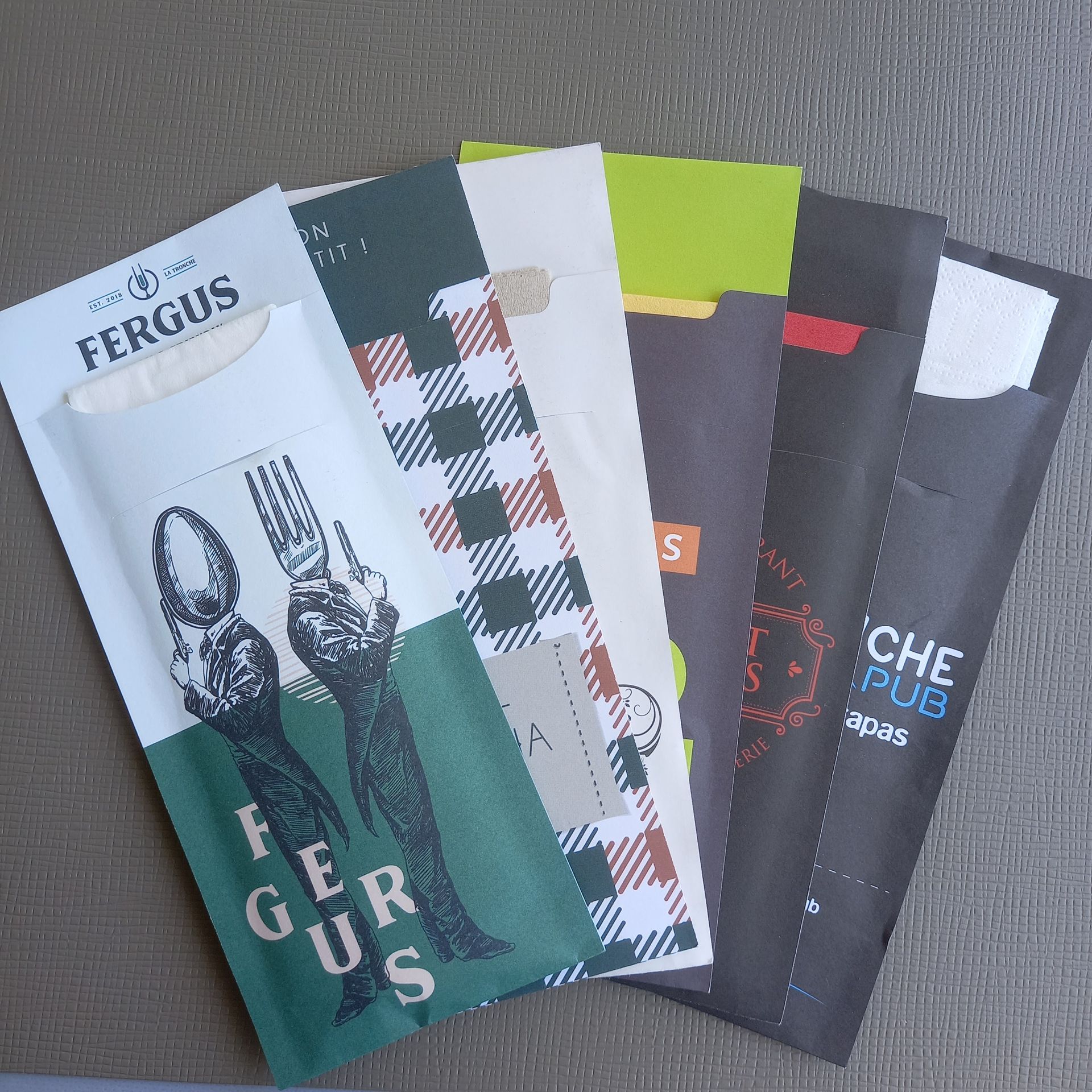 Cinq porte-ustensiles en papier colorés avec des logos de restaurants.