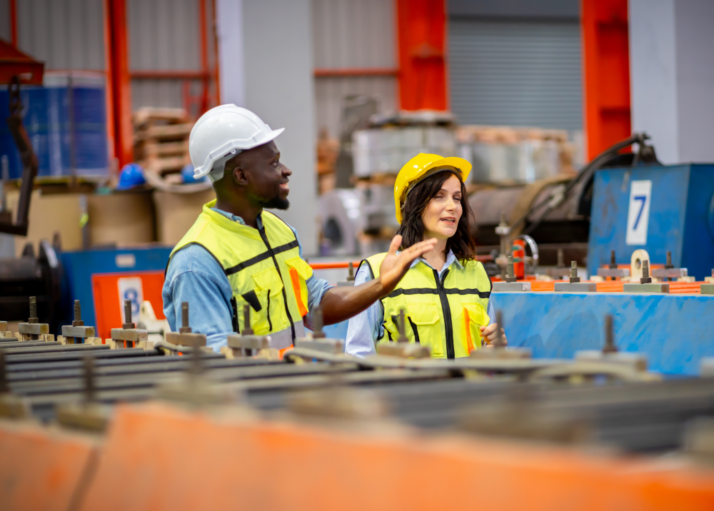 A man and a woman are standing in a factory talking to each other.