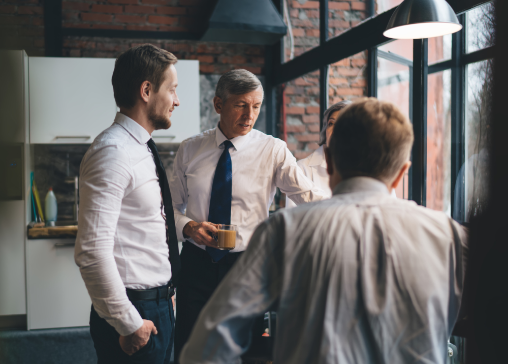 A group of men are standing in front of a window talking to each other.