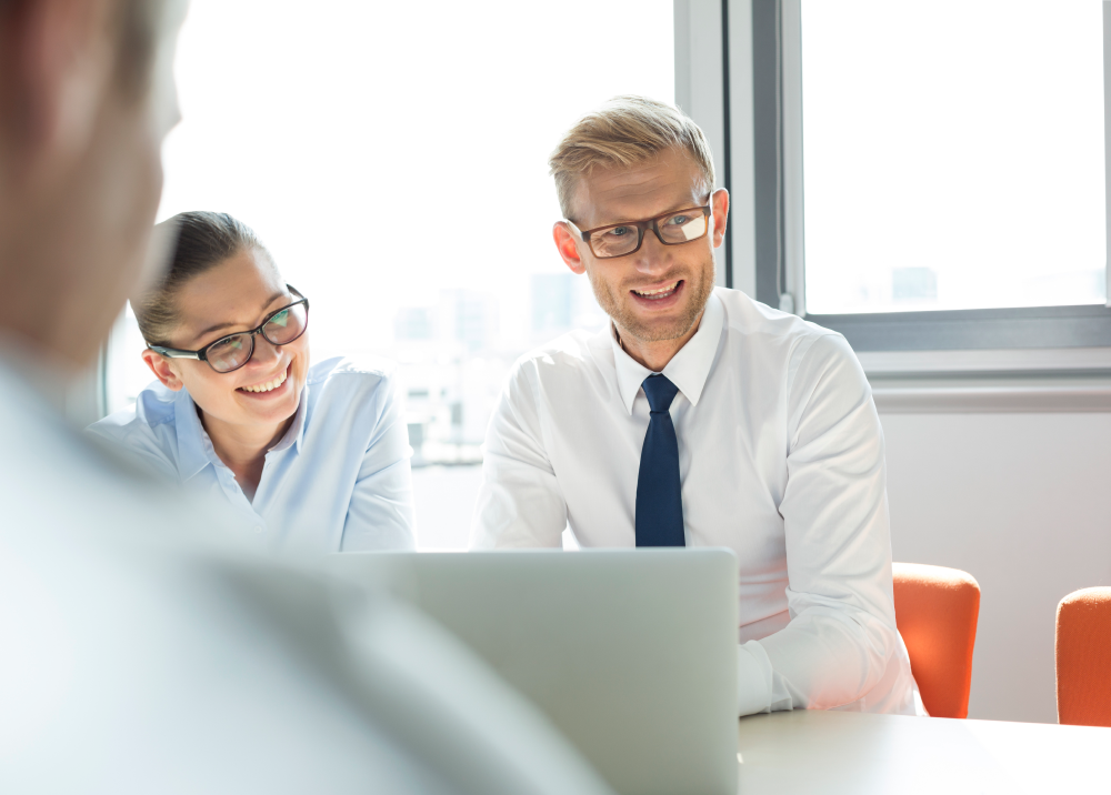 A man and a woman are sitting at a table looking at a laptop computer.