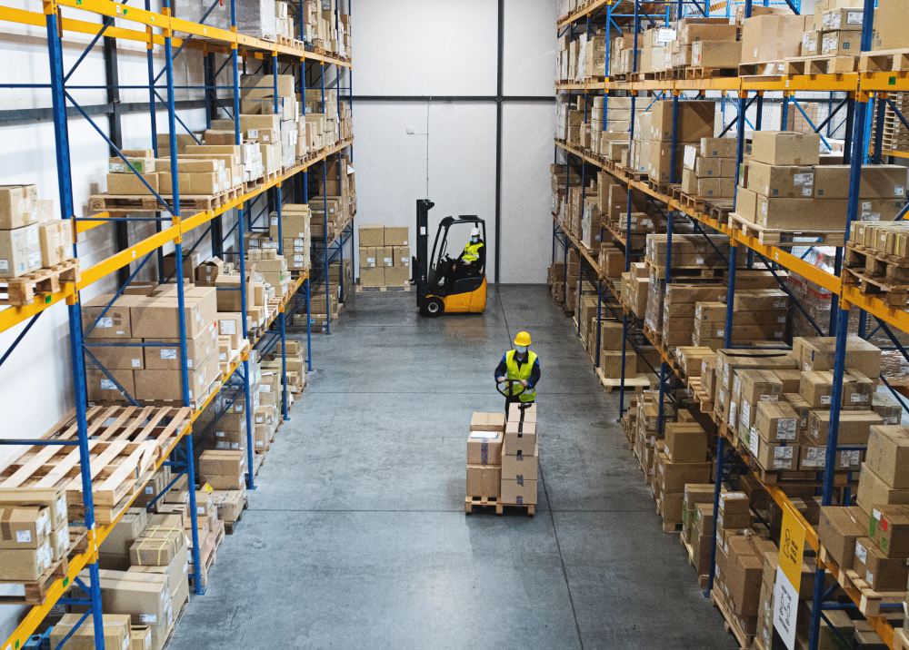 A man is driving a forklift in a warehouse filled with boxes.
