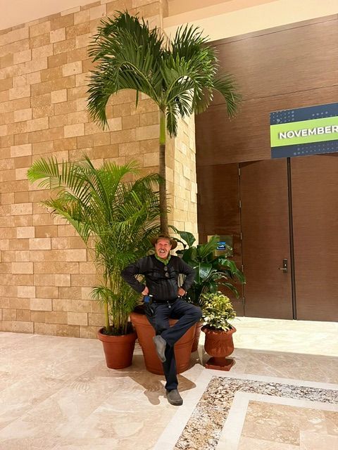 Man sitting next to potted plants in a building lobby.