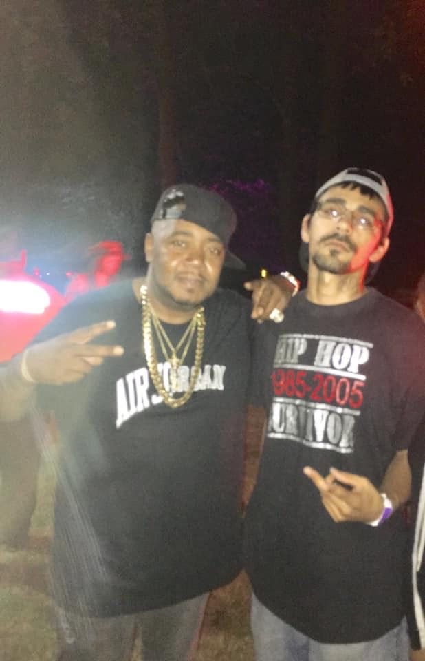 Two men posing for a picture with one wearing a shirt that says hip hop