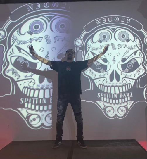 A man stands in front of a projection of a skull that says spittin barz