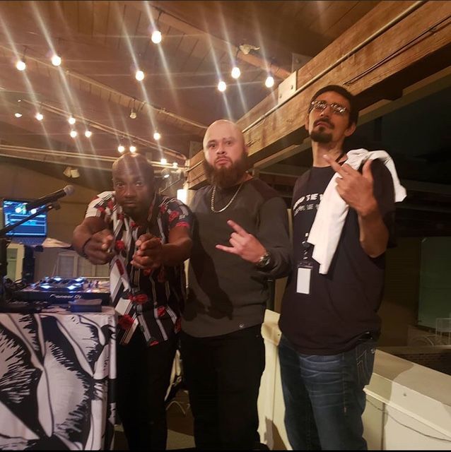 Three men are posing for a picture in front of a dj booth