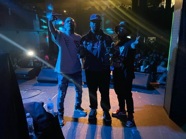 Three men are standing on a stage in front of a crowd.