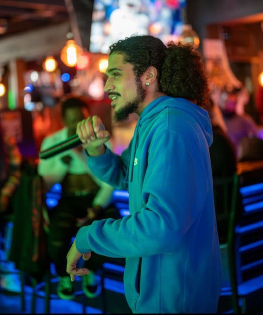 A man in a blue hoodie is singing into a microphone